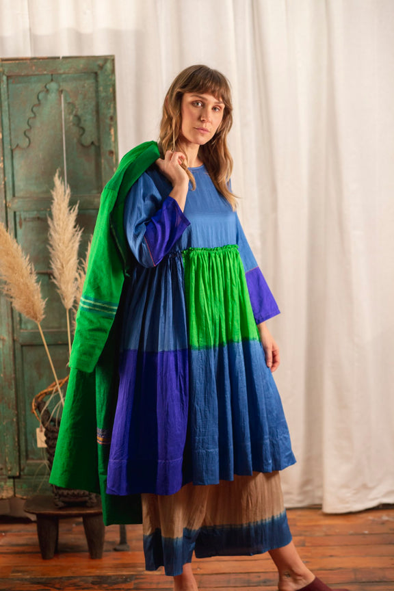Long sleeve blue silk dress with green and purple color block pattern, gathered waist and pleated skirt. On model