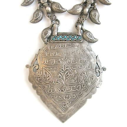 Silver necklace with leaf shaped charms and geometric pendant, close up on pendant