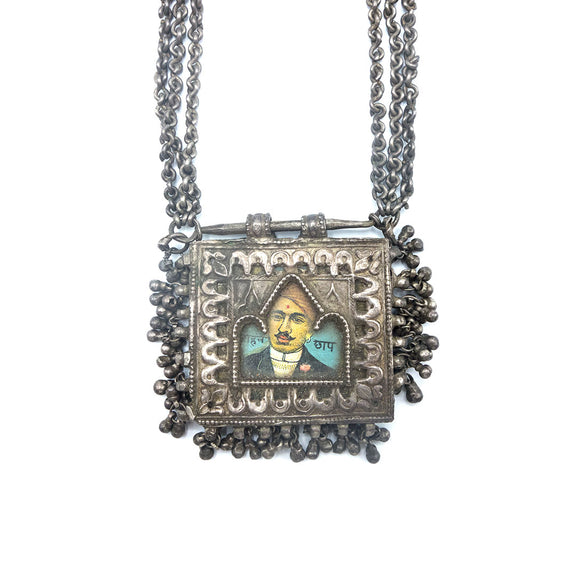 Silver necklace with a picture of a man in the center and small bell charms, close up