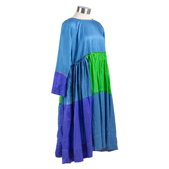 Long sleeve blue silk dress with green and purple color block pattern, gathered waist and pleated skirt. Partial side view