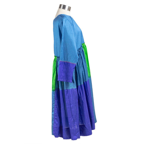 Long sleeve blue silk dress with green and purple color block pattern, gathered waist and pleated skirt. Side view