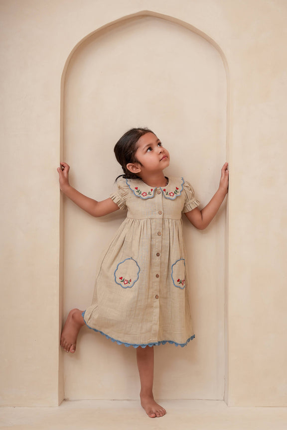 Young girl in a beige dress with floral patterns standing inside an archway.