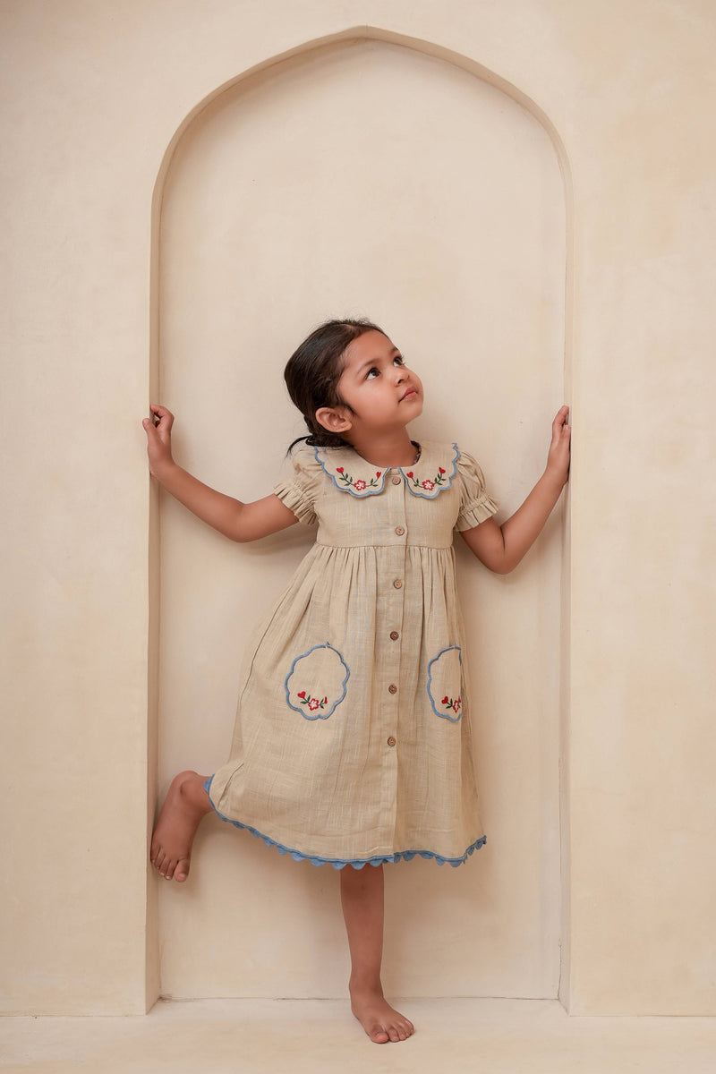 Young girl in a beige dress with floral patterns standing inside an archway.