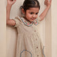Young girl wearing a beige dress with floral embroidery against a plain background