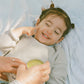 Child lying down with a person applying cream to their face, both on a light blue blanket.