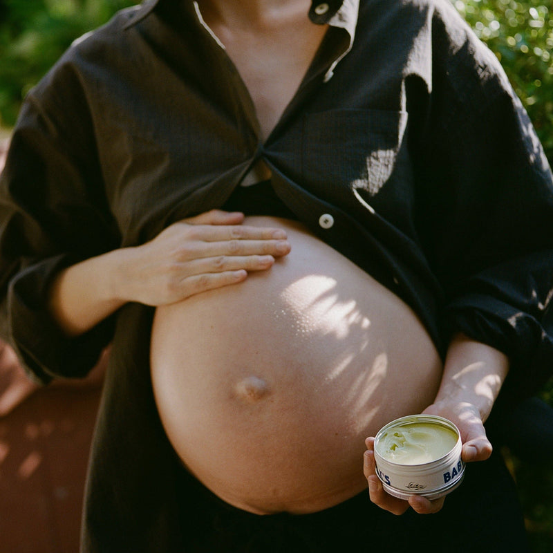 Pregnant person holding a container of Dr. Max baby balm.