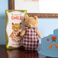 Teddy bear in a checkered dress next to its packaging with 'Bèbe Emile' branding.