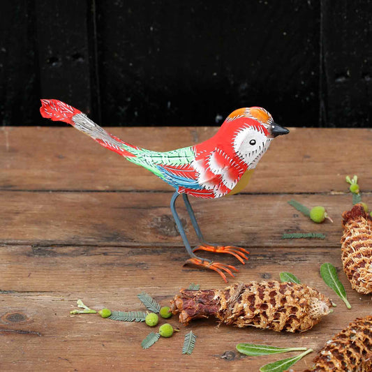 Colorful bird figurine on a wooden surface with pine cones and leaves.