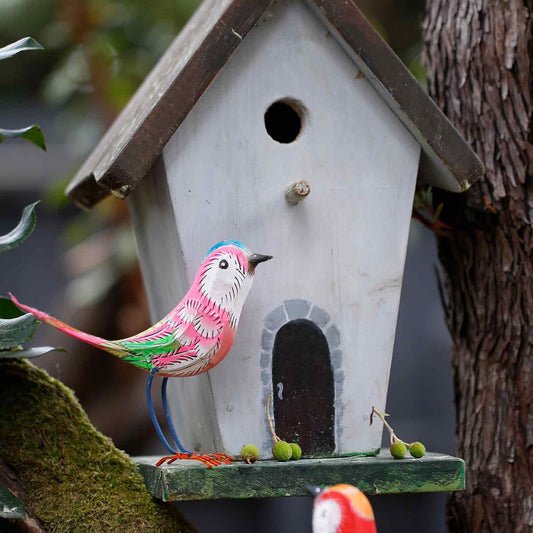 Decorative birdhouse with a colorful bird figurine attached, set against a natural background.
