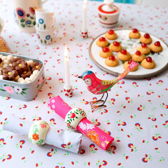Table setting with decorative items, candles, and a small bird figurine on a floral tablecloth.