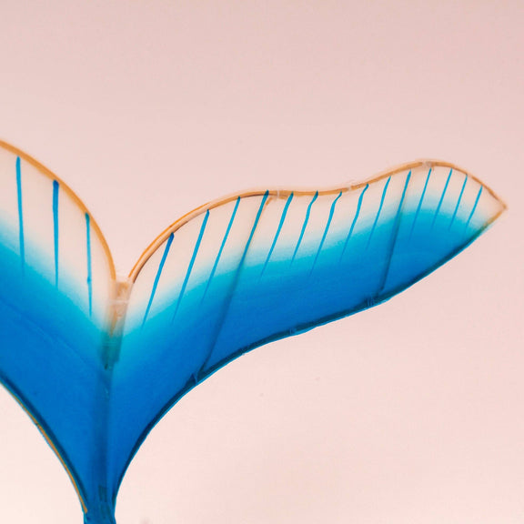 Close-up of a blue and gold mermaid tail on a pink background
