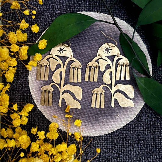 Gold floral earrings on a dark fabric background with yellow flowers and green leaves.