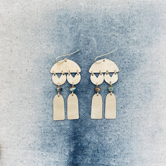Pair of gold earrings with hanging elements on a textured blue background