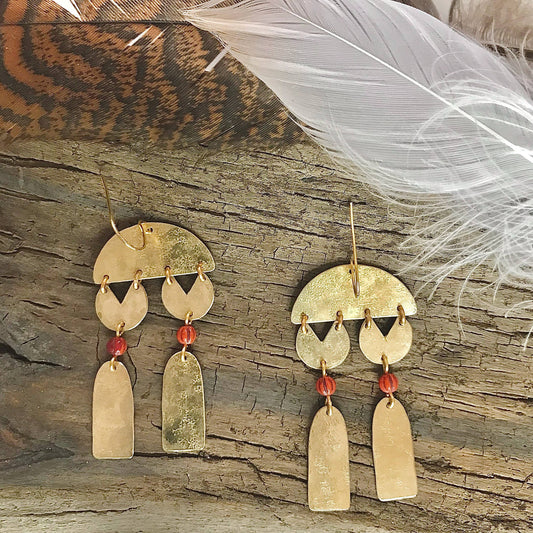 Pair of gold earrings with red beads on a wooden surface with a feather.