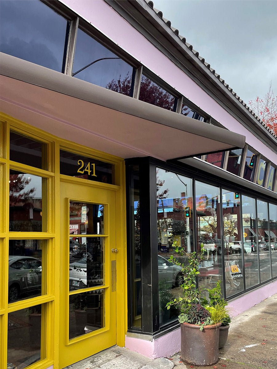 The front of a store with a yellow door, purple walls and glass windows.