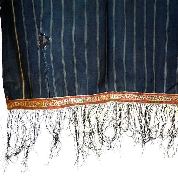 Cotton indigo colored batak with subtle stripe pattern, orange trim and black tassels. Close up