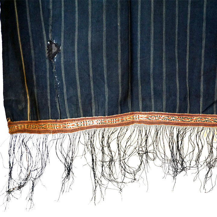 Cotton indigo colored batak with subtle stripe pattern, orange trim and black tassels. Close up