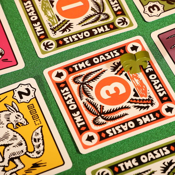 Close-up of playing cards with 'The Oasis' design on a green fabric background