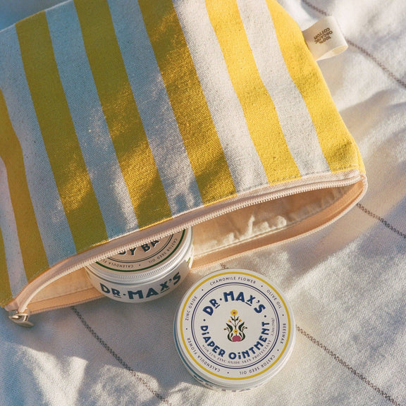 Two jars of Dr. Max's Diaper Ointment on a striped towel with a pouch.