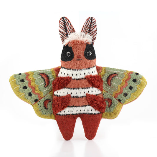Knitted toy resembling a butterfly with red and white stripes on a white background