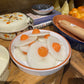 Bowl of sliced egg candles with yolks on a wooden table with cookbooks and a rolling pin.