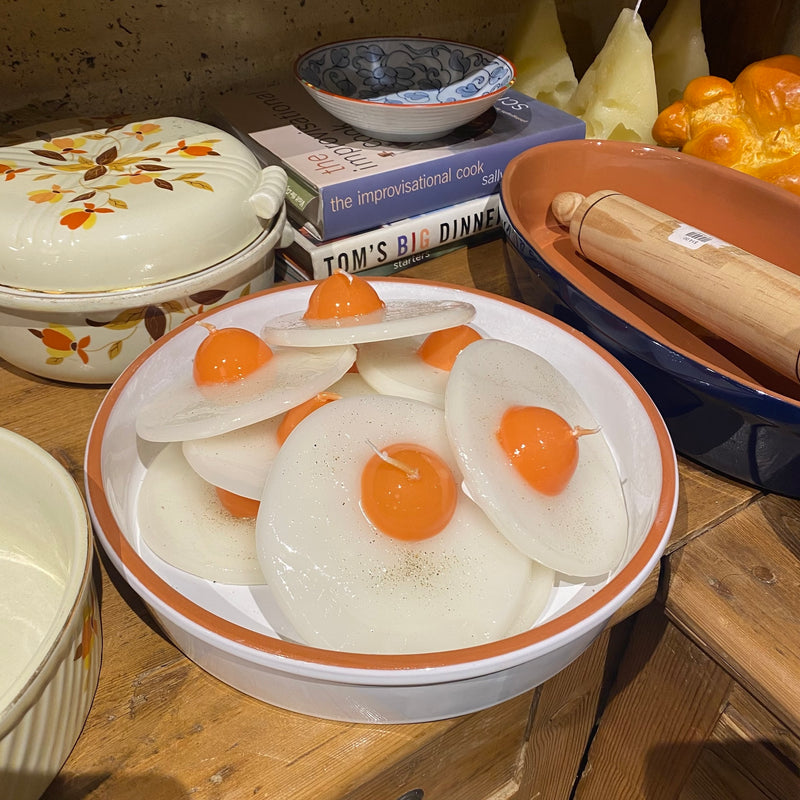 Bowl of sliced egg candles with yolks on a wooden table with cookbooks and a rolling pin.