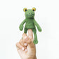 Green frog finger puppet on a person's finger against a white background