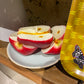 Sliced candle apples on a white plate with a yellow paper plate featuring a butterfly design in the background.