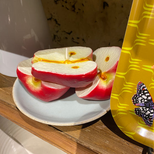 Sliced candle apples on a white plate with a yellow paper plate featuring a butterfly design in the background.