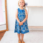 Young girl wearing a blue floral dress standing in a room with a mirror and white wall.