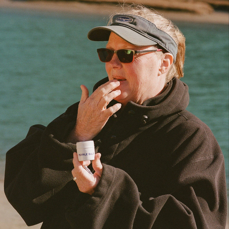 Person holding a bottle of Ruffle Butts clothing brand by a body of water.