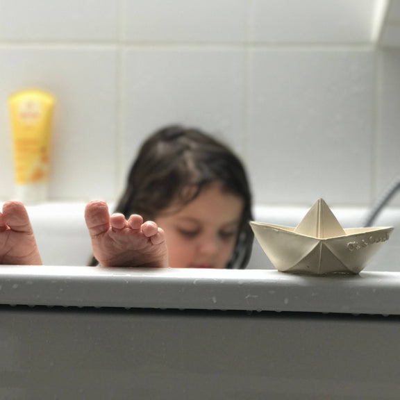 Child in a bathtub with a paper boat and a candle in the background