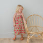 Young girl in a floral dress standing next to a wicker chair against a plain wall.