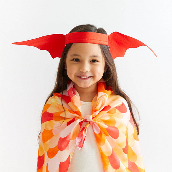 Child wearing a colorful cape and red headband with wing-like design on a white background
