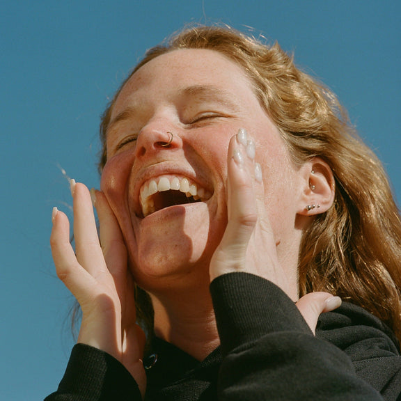 Person laughing with hands on face against a clear blue sky
