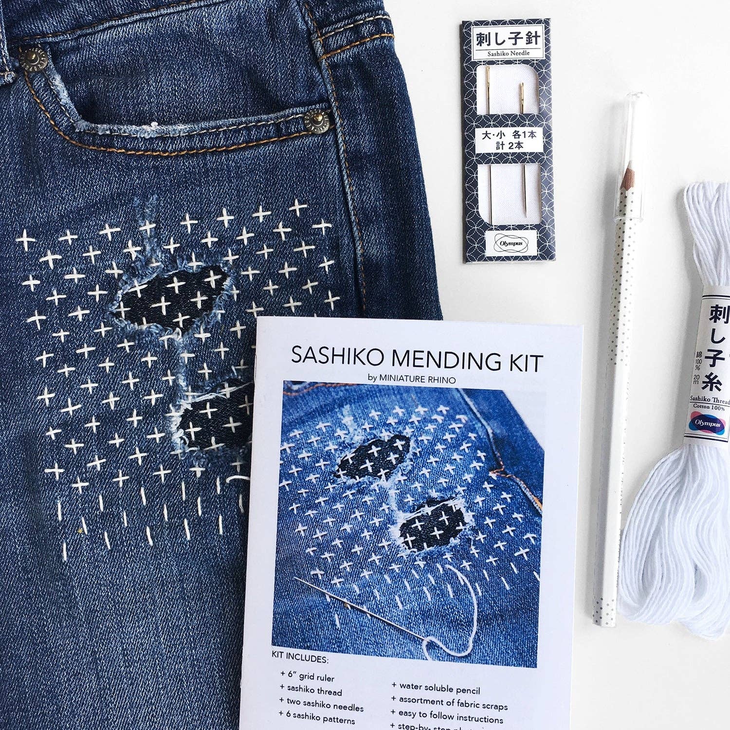Sashiko mending kit with denim fabric, needles, and thread on a white background