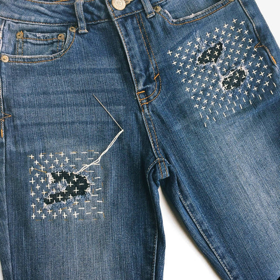 Blue jeans with decorative stitching patterns on a white background