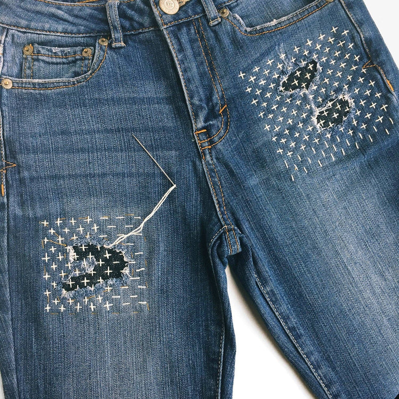 Blue jeans with decorative stitching patterns on a white background