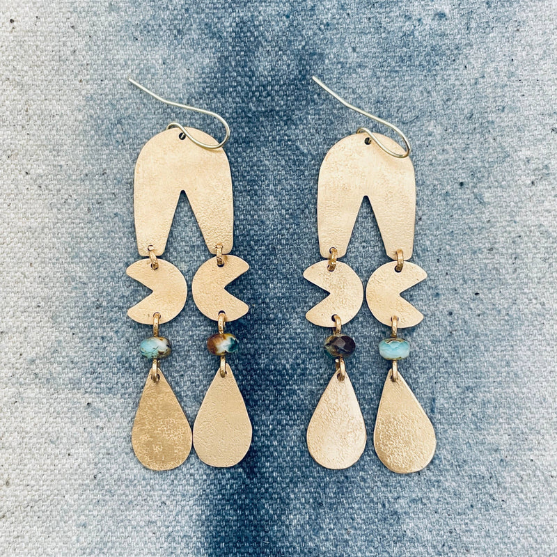Pair of gold earrings with teardrop and crescent moon shapes on a textured blue background