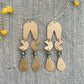 Pair of gold earrings on a textured gray surface with yellow flowers.