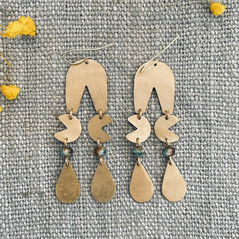 Pair of gold earrings on a textured gray surface with yellow flowers.