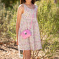 Young girl wearing a floral dress with a pink crossbody bag outdoors.