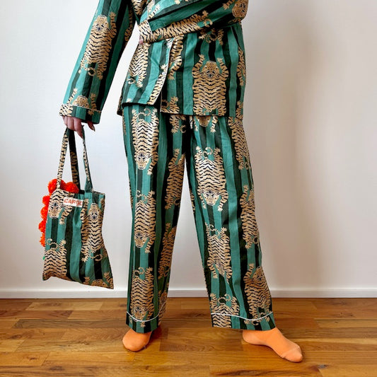 Person wearing a green and gold patterned outfit holding a matching bag on a wooden floor.