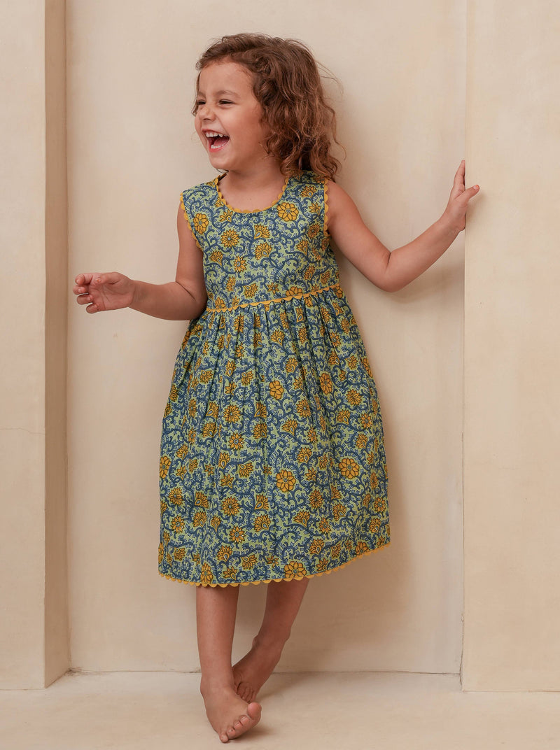 Child wearing a floral dress standing against a plain background