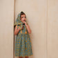 Child wearing a floral dress with a hood in front of an archway.
