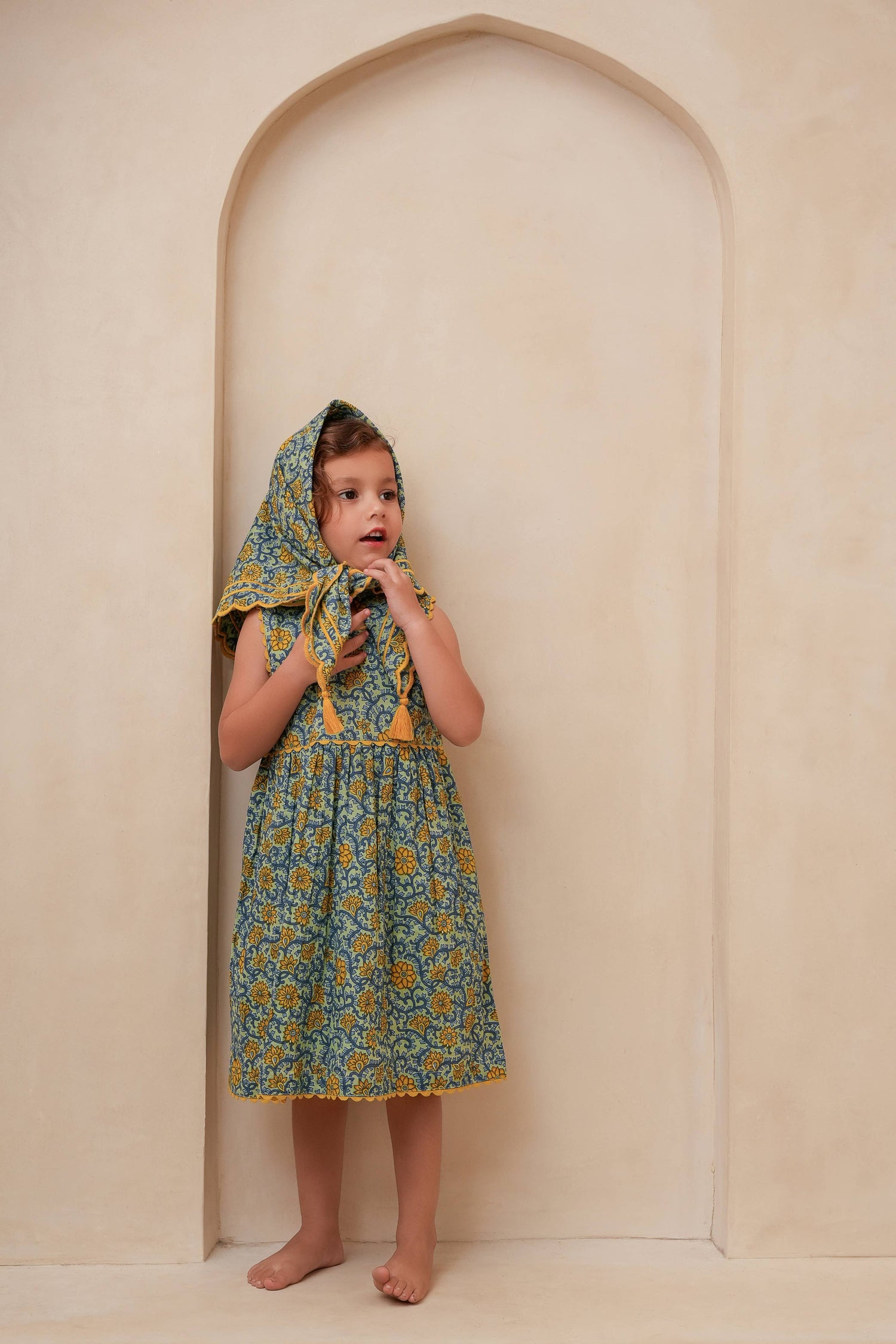 Child wearing a floral dress with a hood in front of an archway.