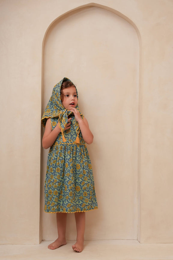 Child wearing a floral dress with a hood in front of an archway.