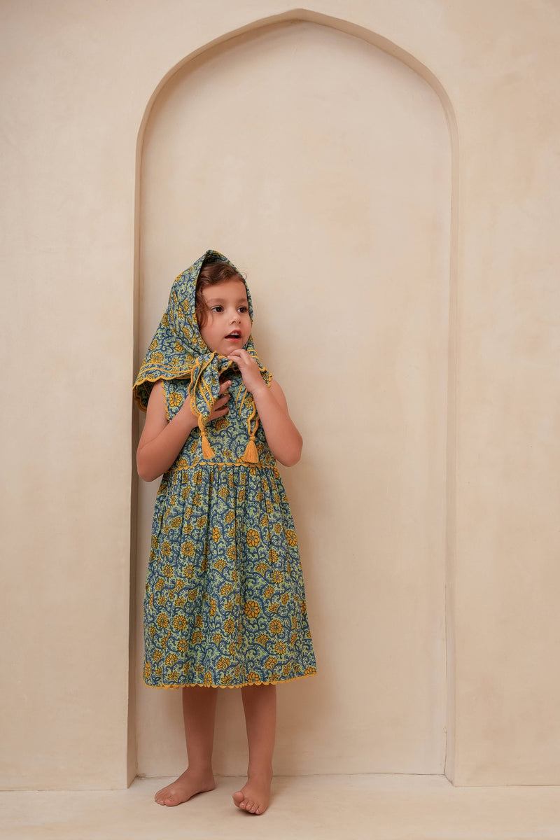 Child wearing a floral dress with a hood in front of an archway.