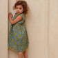 Young girl in a floral dress standing against a plain wall