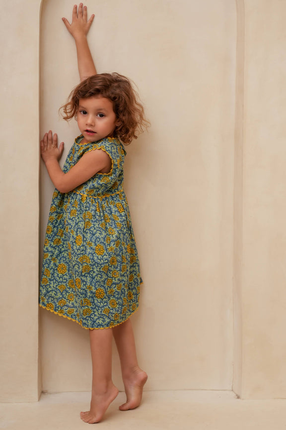 Young girl in a floral dress standing against a plain wall